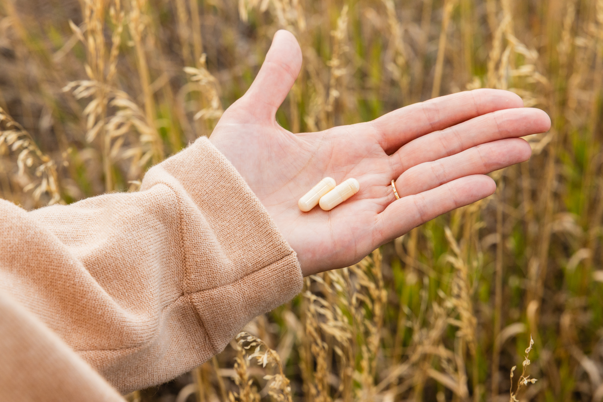 Hand holding two capsules in an outdoor grassy setting.