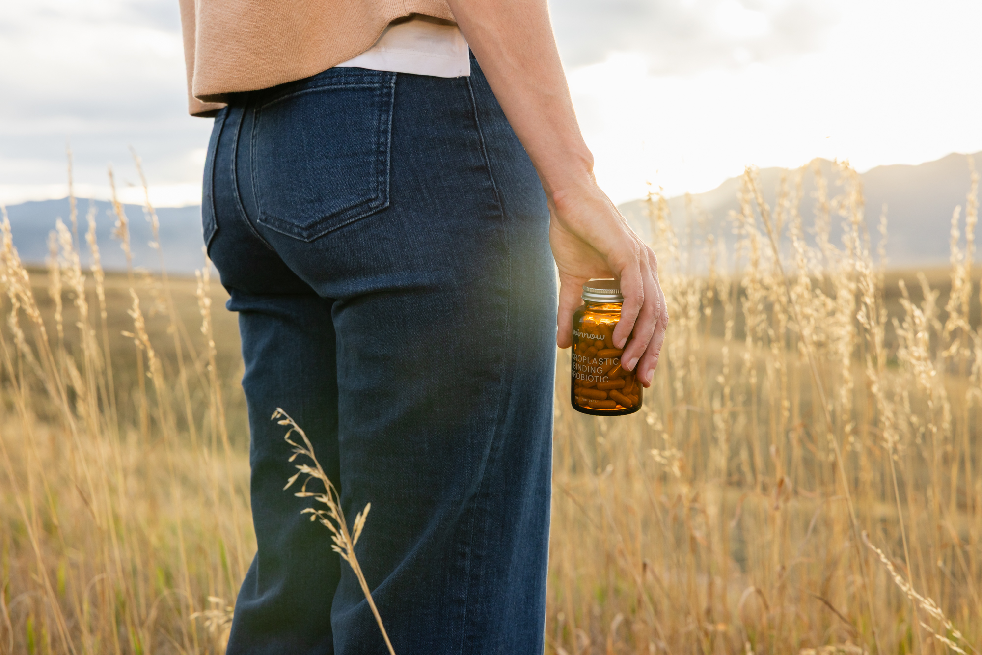 Person holding a brown bottle in a grassy field at sunset.