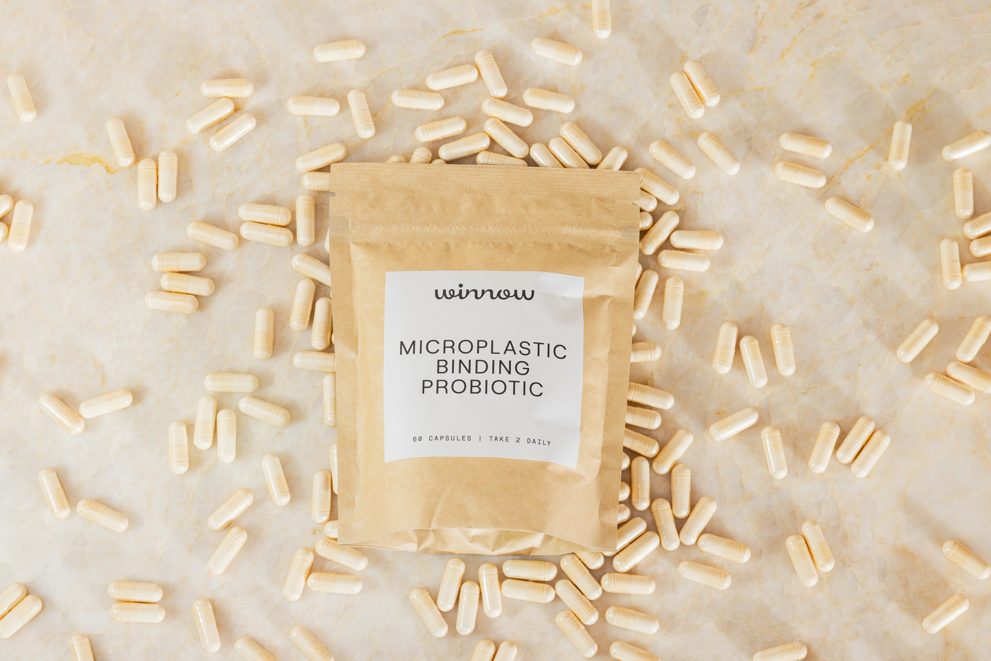 Bag labeled 'microplastic binding probiotic' surrounded by capsules on marble surface.