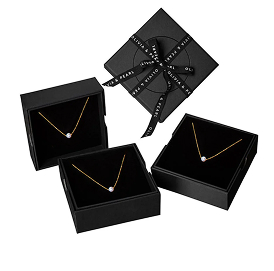 Three black jewelry boxes with gold necklaces, one wrapped with ribbon.