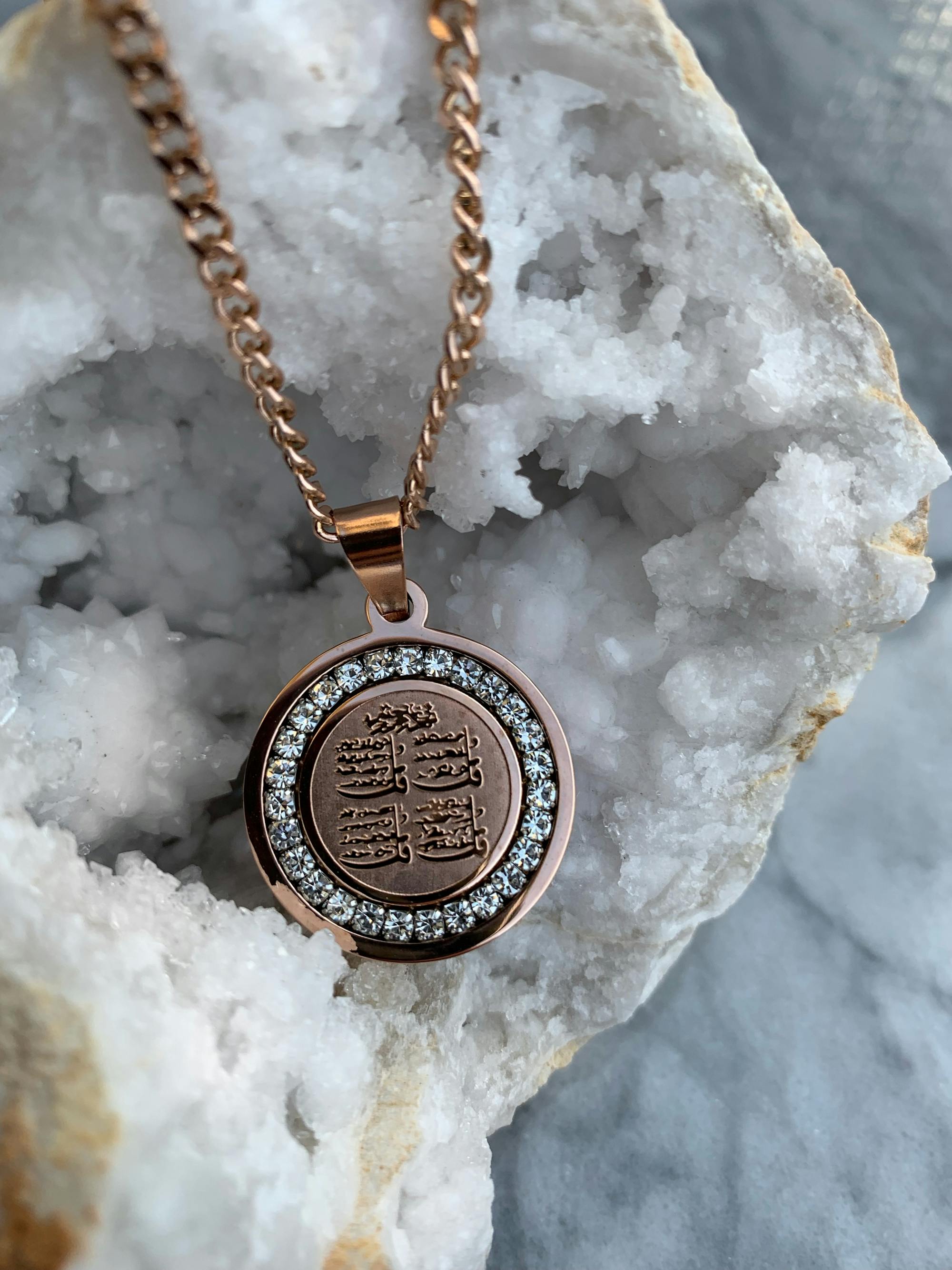 Gold pendant with intricate design on a chain, placed on a white crystal.