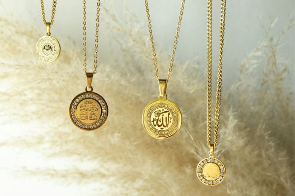 Five gold necklaces with round pendants on a soft, blurred background.