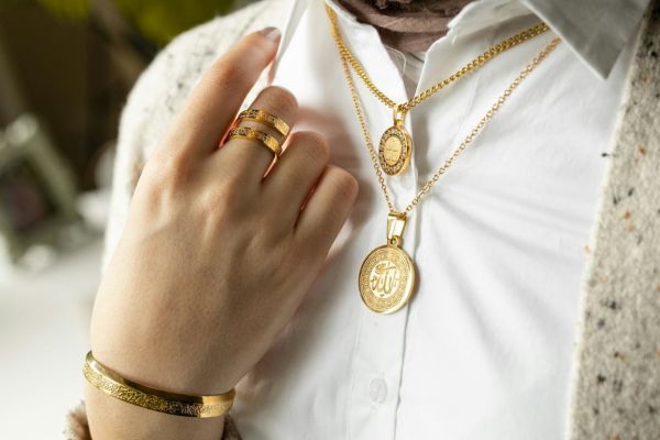 Person wearing gold jewelry including necklaces, rings, and a bracelet.