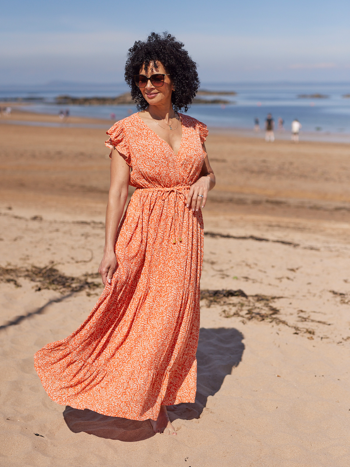 Person in orange dress standing on a sandy beach with ocean in background.