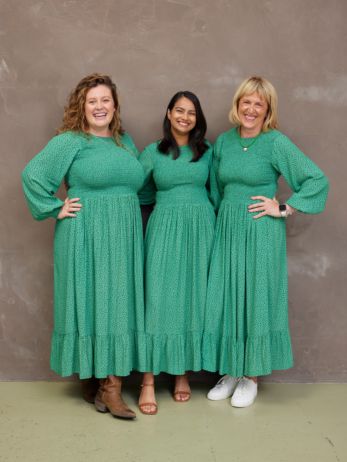 Three women in matching green dresses smiling at the camera.