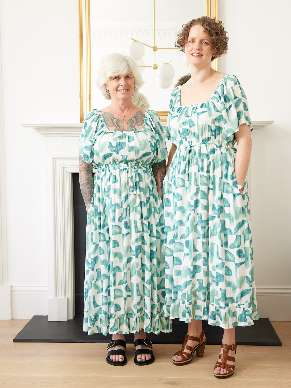 Two people in matching patterned dresses standing in a bright room.