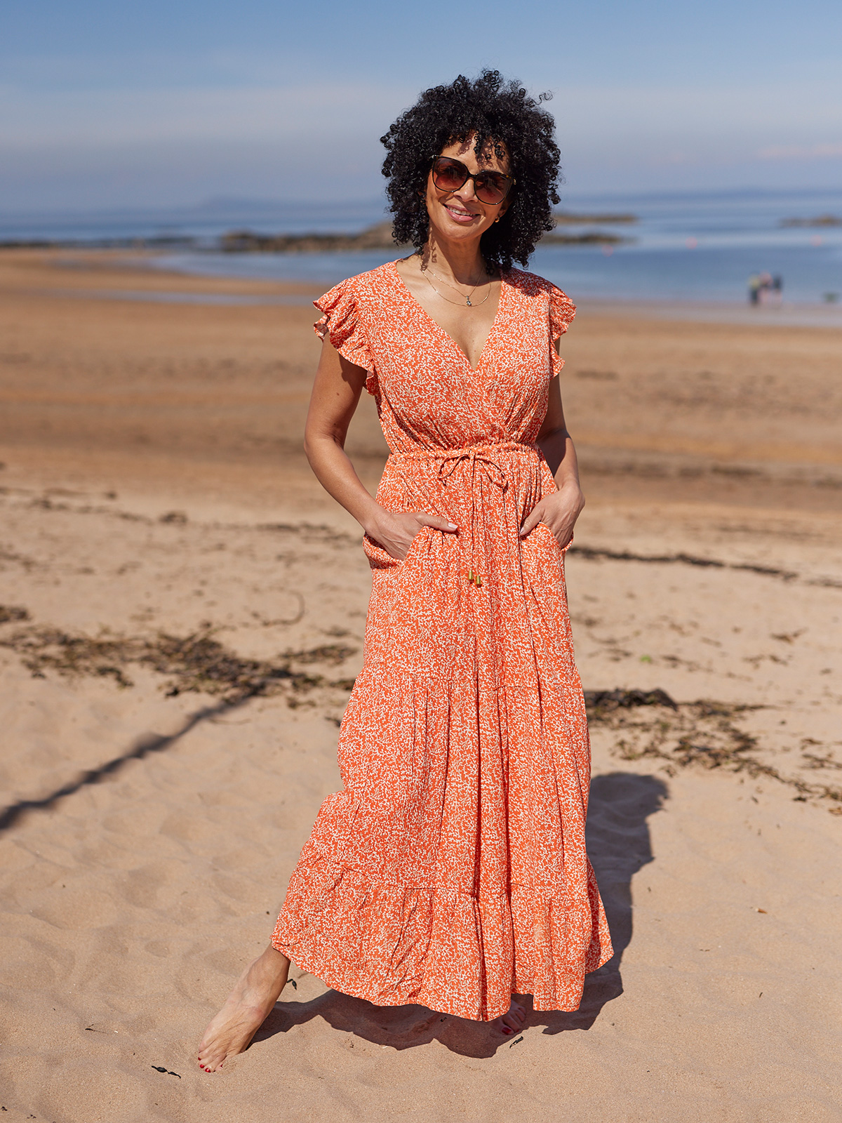 Person in orange dress standing on a sunny beach.