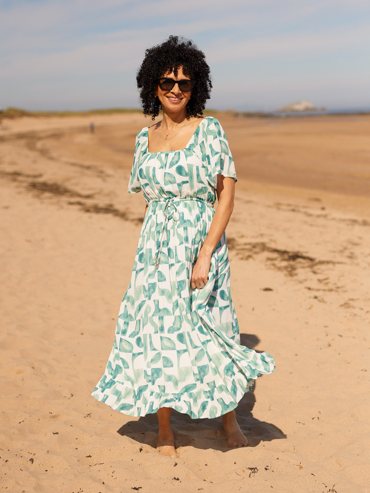 Person in a patterned dress standing on a sandy beach.