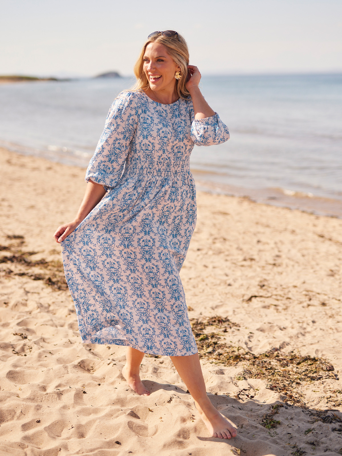 Woman in floral dress walking on a sunny beach.