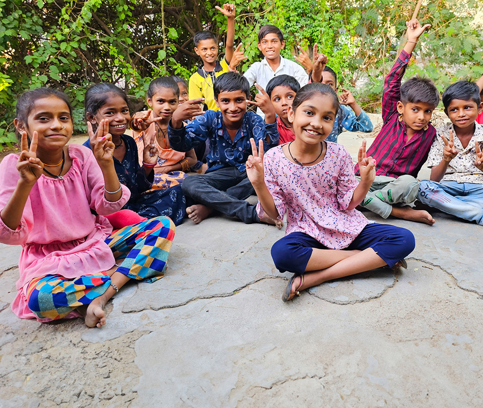 Group of smiling children sitting outdoors, making peace signs.