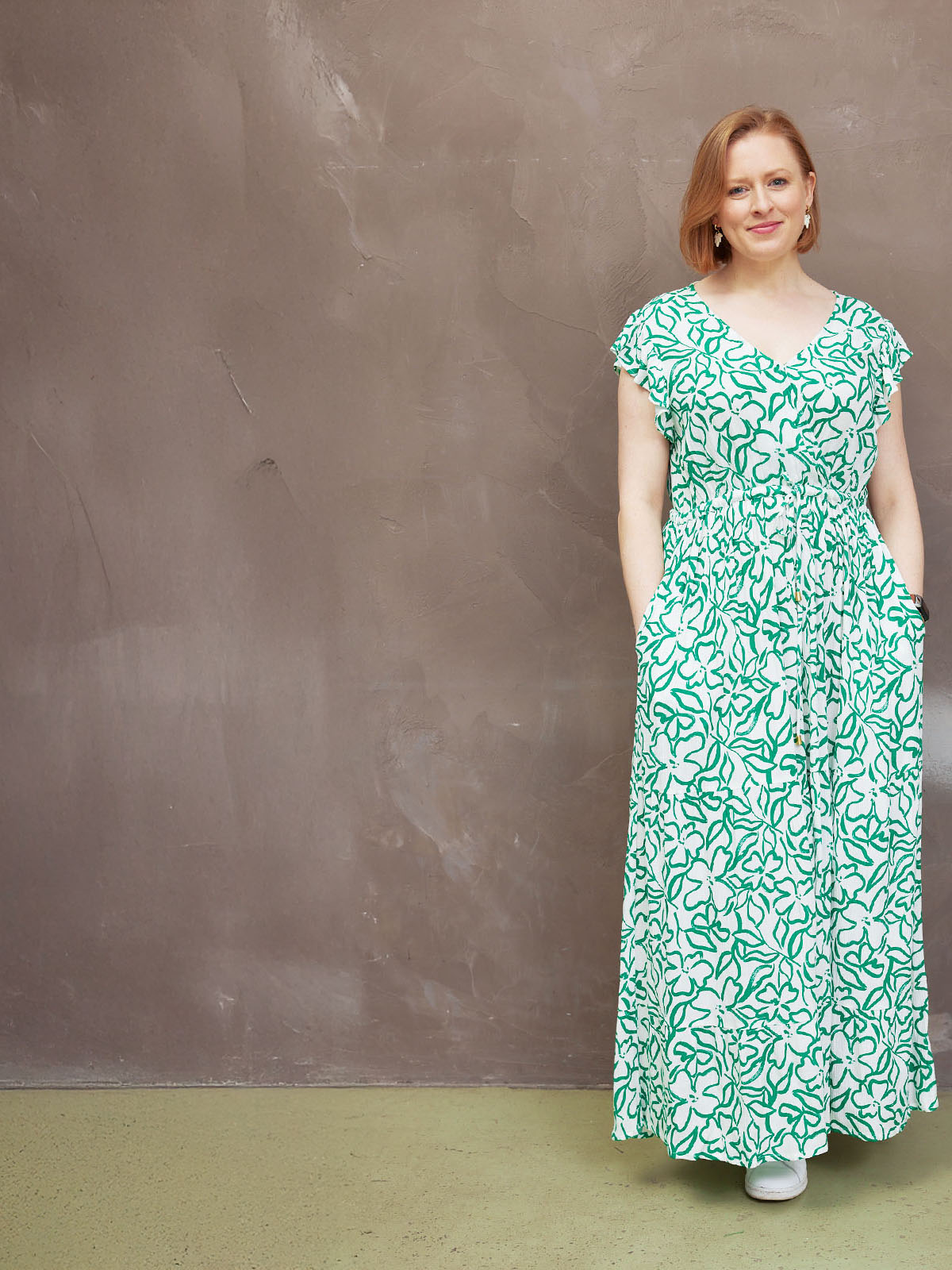 Woman in a green floral dress against a brown textured wall.