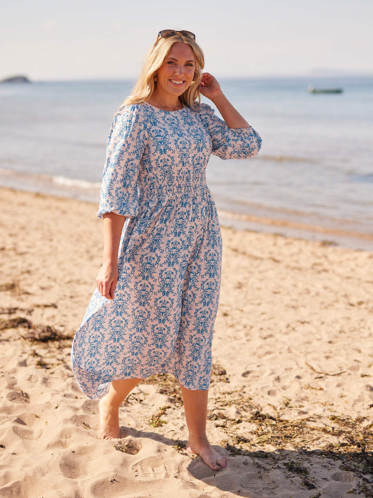 Woman in a floral dress walking on a sandy beach.