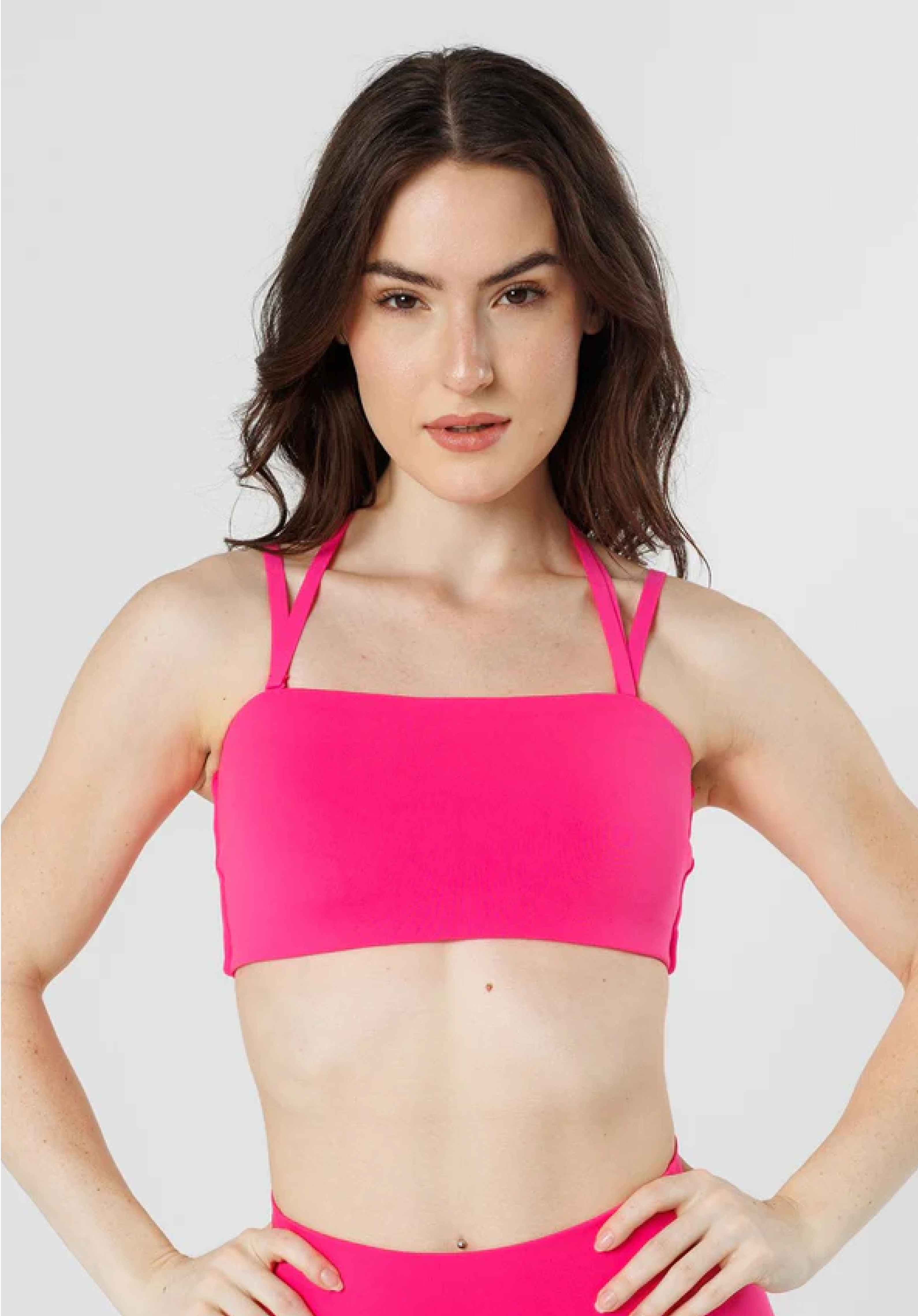 A woman with long dark hair models a hot pink bandeau-style sports bra against a white background.
