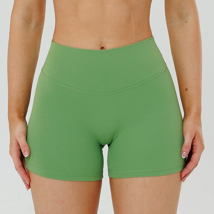 A close-up front view of a person wearing high-waisted green shorts against a white background.