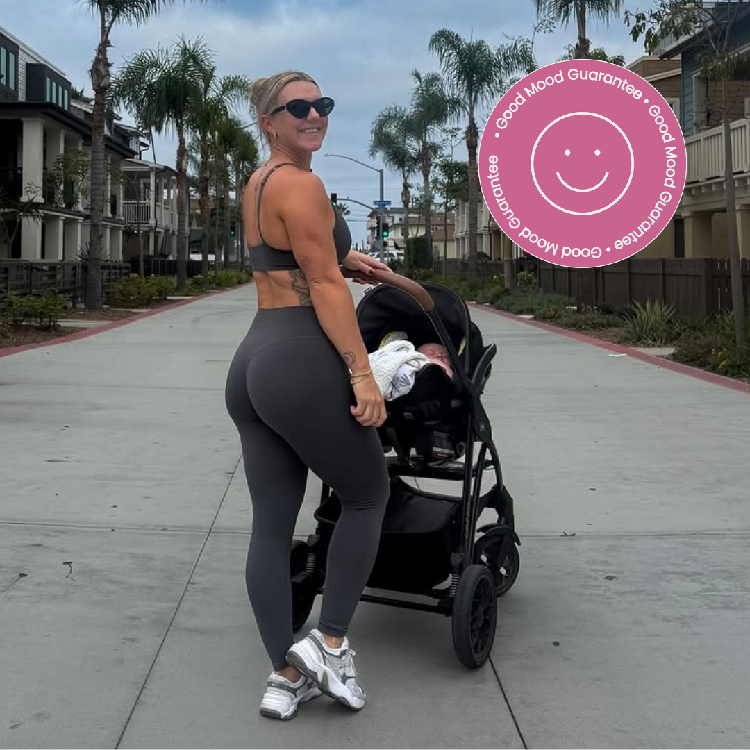 A smiling woman in workout clothes pushes a baby stroller on a palm tree-lined street.