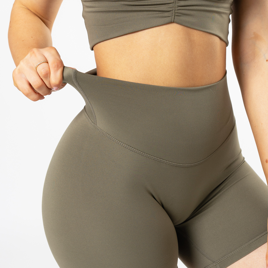 Person wearing olive green high-waisted shorts and crop top, adjusting waistband.