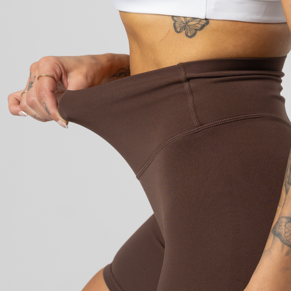Person stretching brown leggings, showing tattooed arm and torso.
