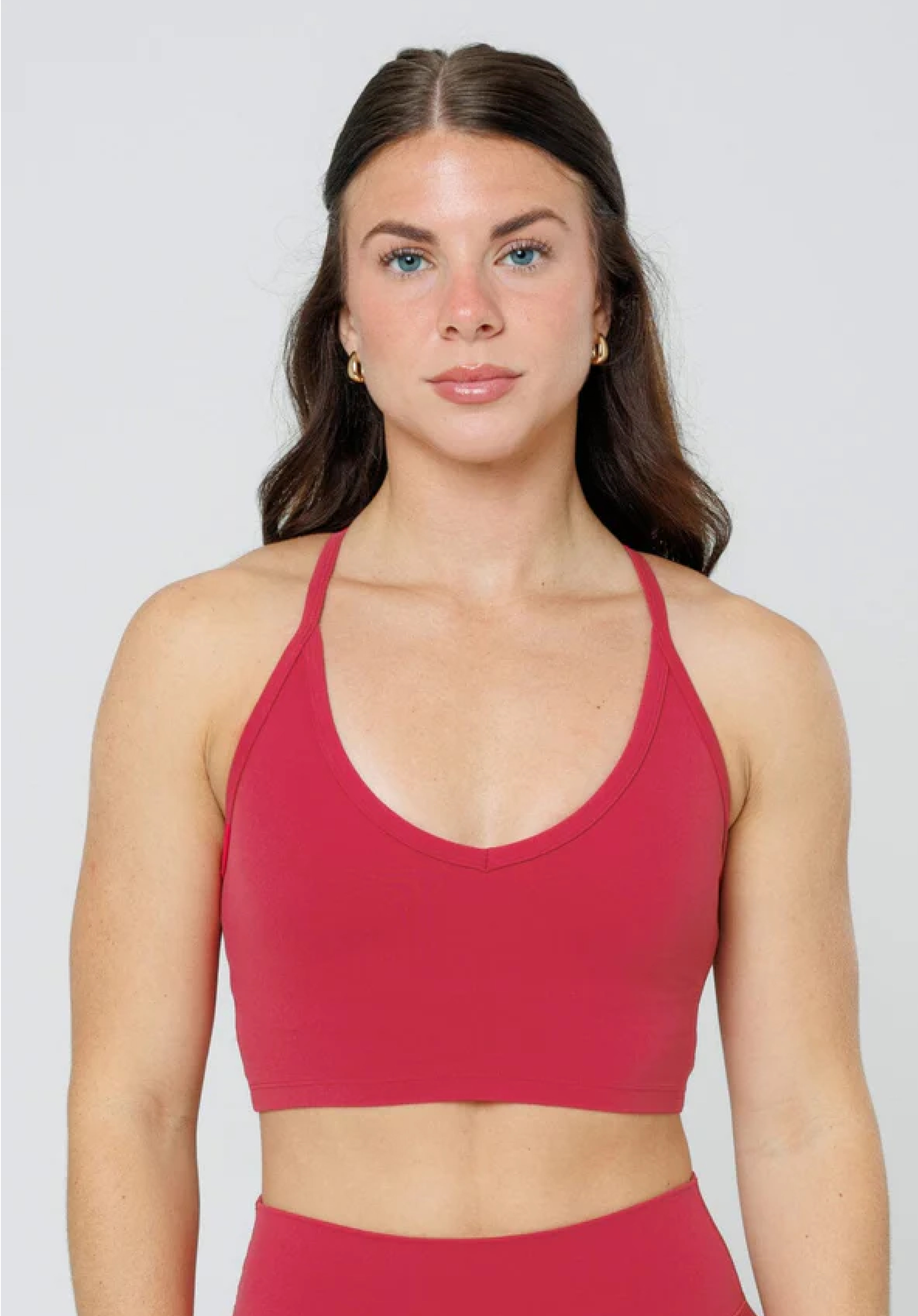 A woman with brown hair and blue eyes wearing a red sports bra and matching bottoms.