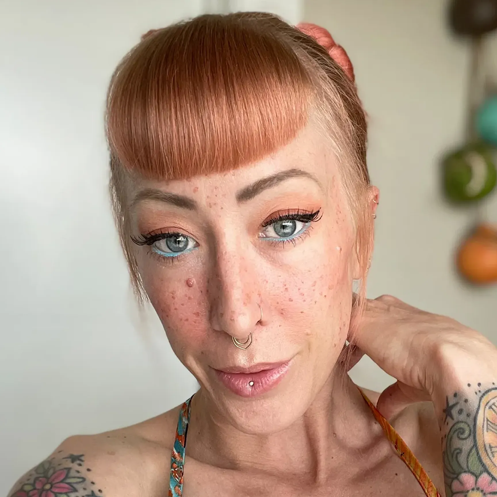 A close-up of a woman with pink hair, blue eyeliner, freckles, facial piercings, and tattoos.