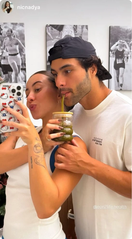 A woman takes a selfie with a man who is drinking a green beverage from her glass.