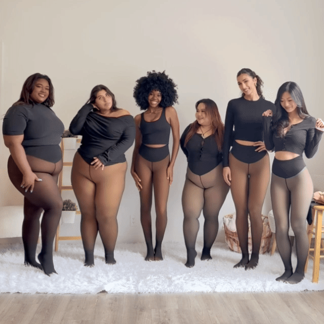 Group of six women in black outfits and sheer tights, standing on a white rug.