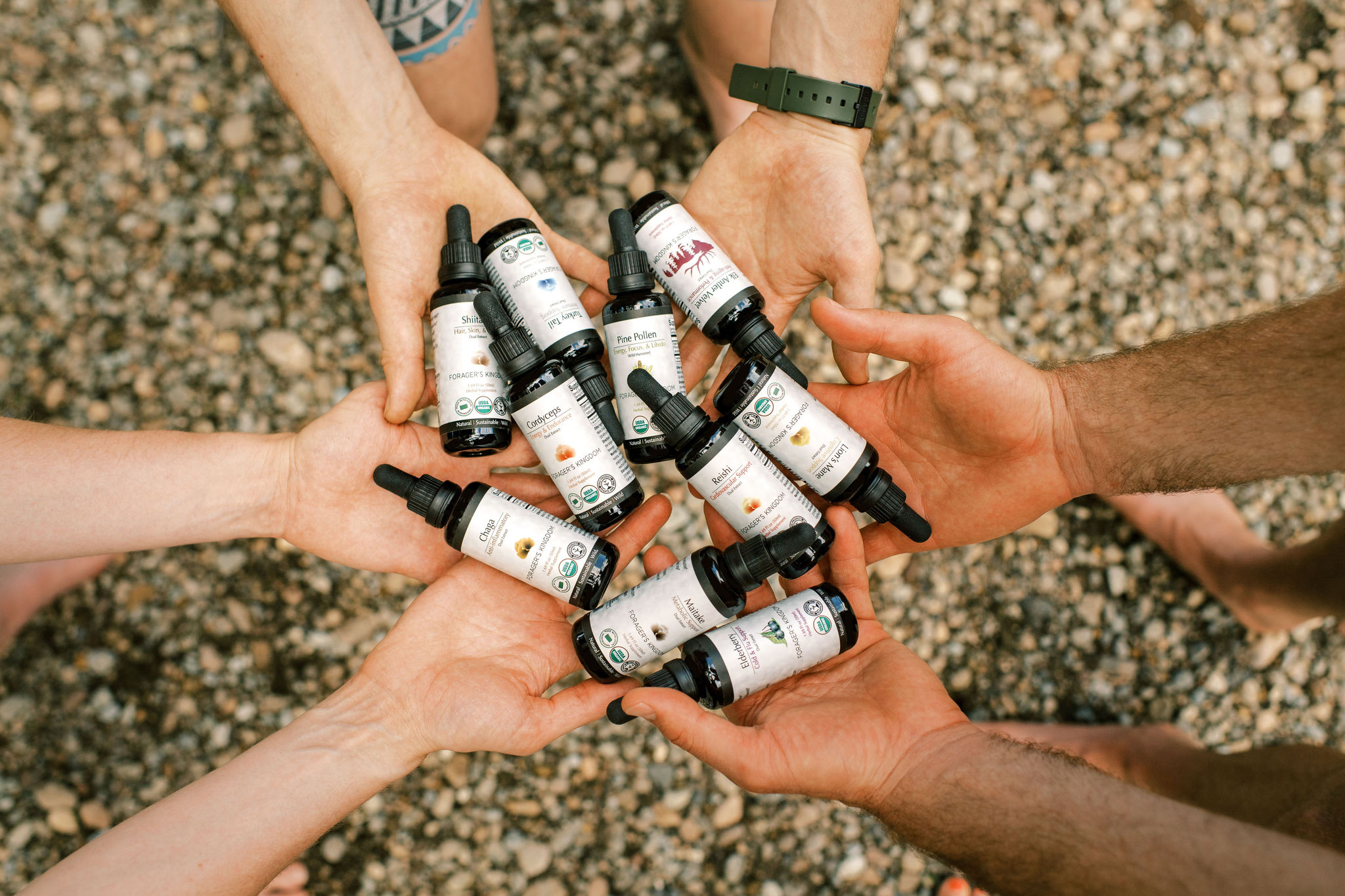 Hands holding multiple dropper bottles over a gravel background.