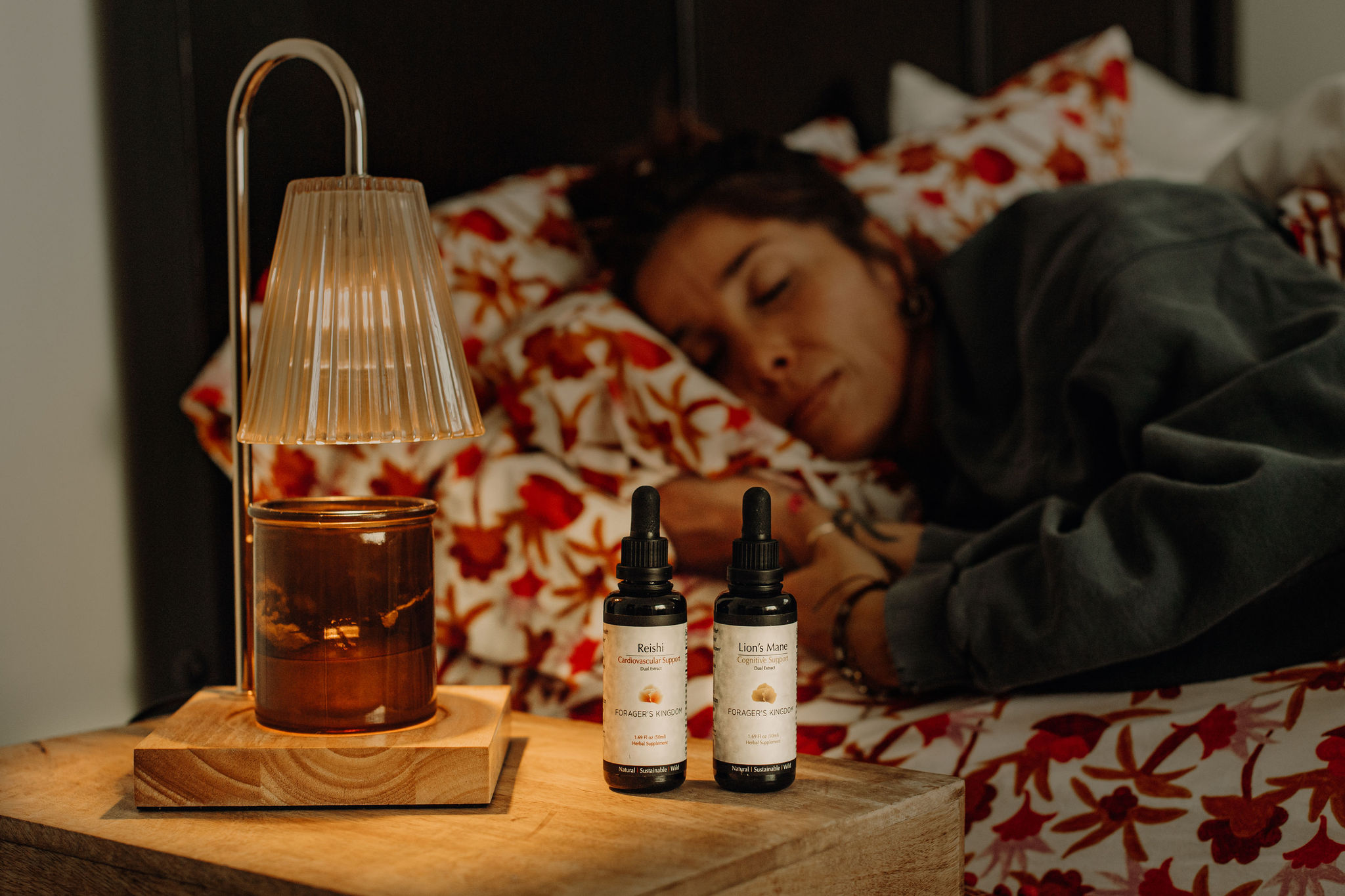 Two dropper bottles and a lamp on a nightstand next to a woman sleeping in bed.