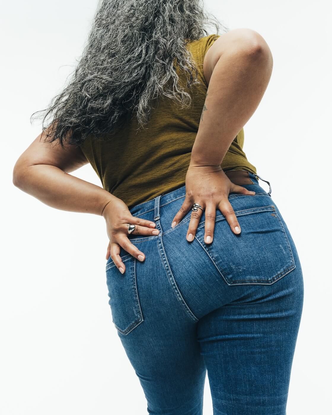 A person with long gray hair, seen from behind, with their hands placed on their lower back.