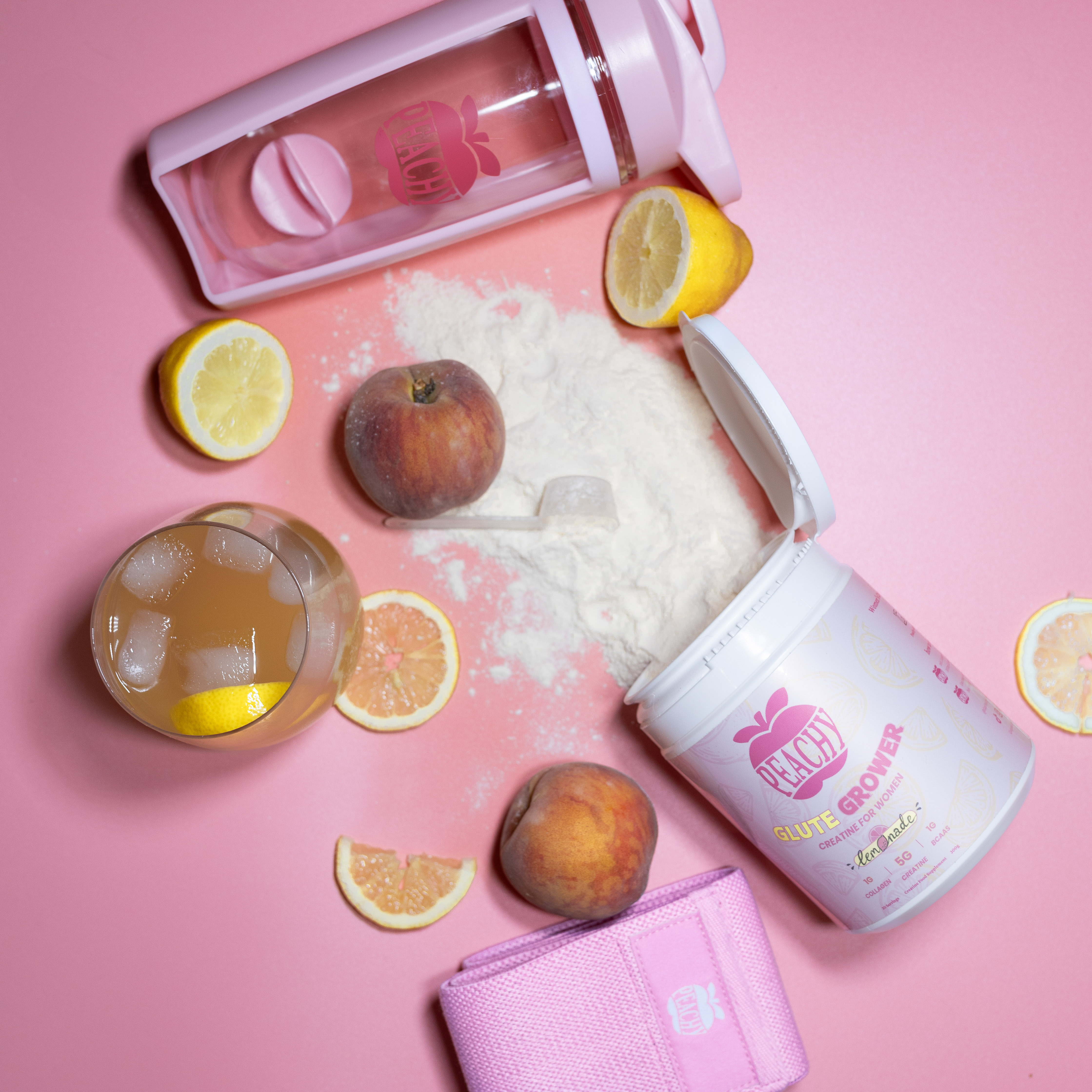 Fitness powder, peach, lemon slices, drink, pink shaker, and strap on a pink background.