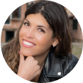 Smiling person with long hair wearing a leather jacket, outdoors.