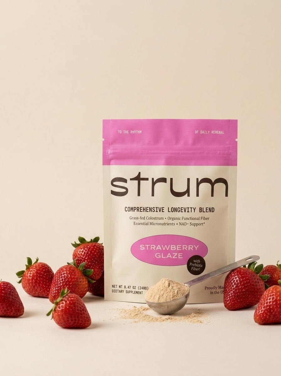 A pouch of Strum Strawberry Glaze supplement powder with a scoop and fresh strawberries.