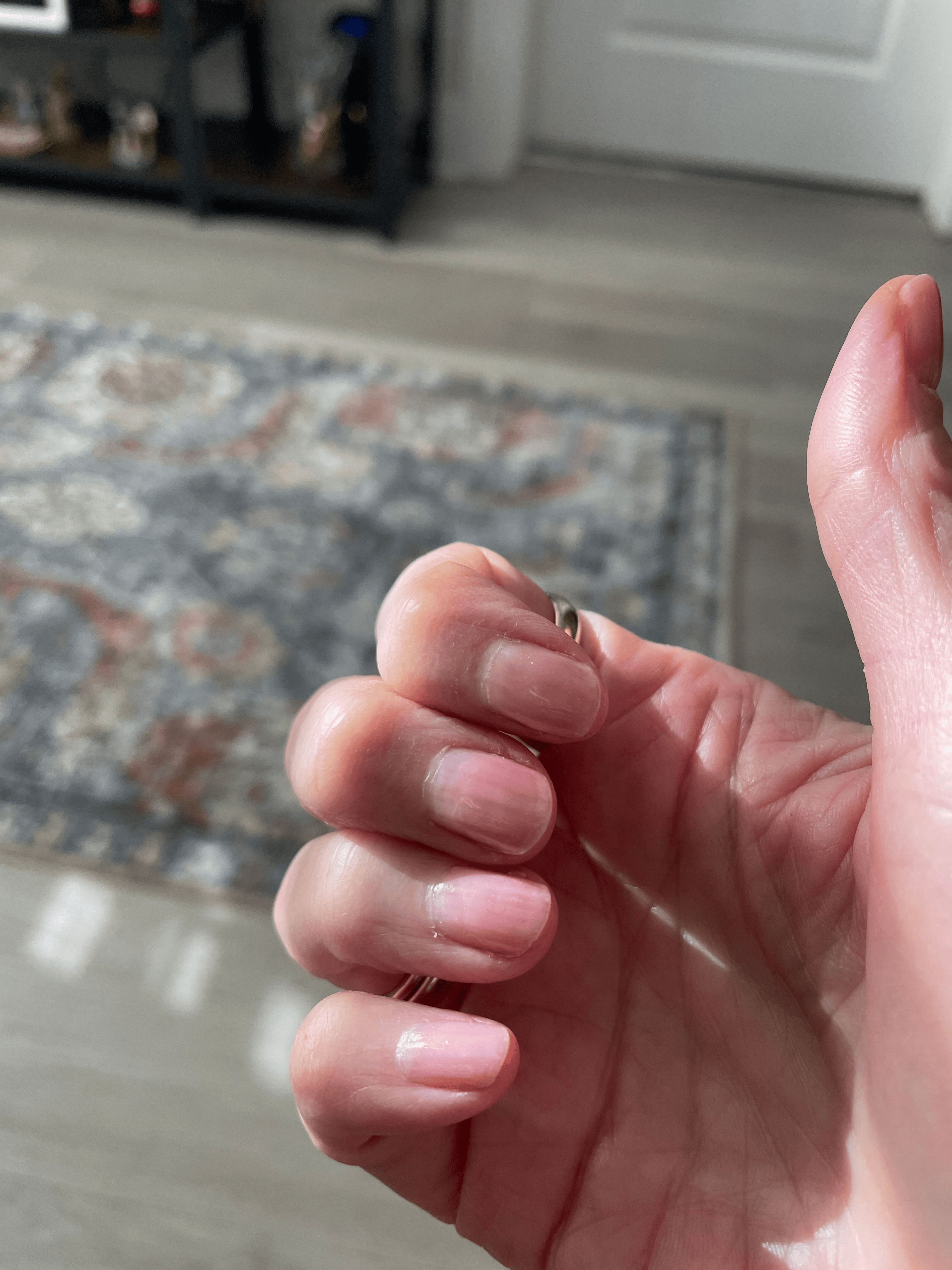 A close-up of a hand with light pink manicured nails and a thumb held up.