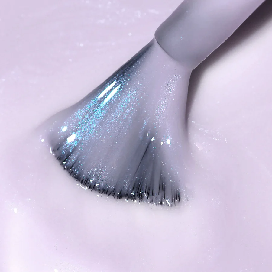 A close-up of a nail polish brush fanned out in a shimmery, pale lavender polish.