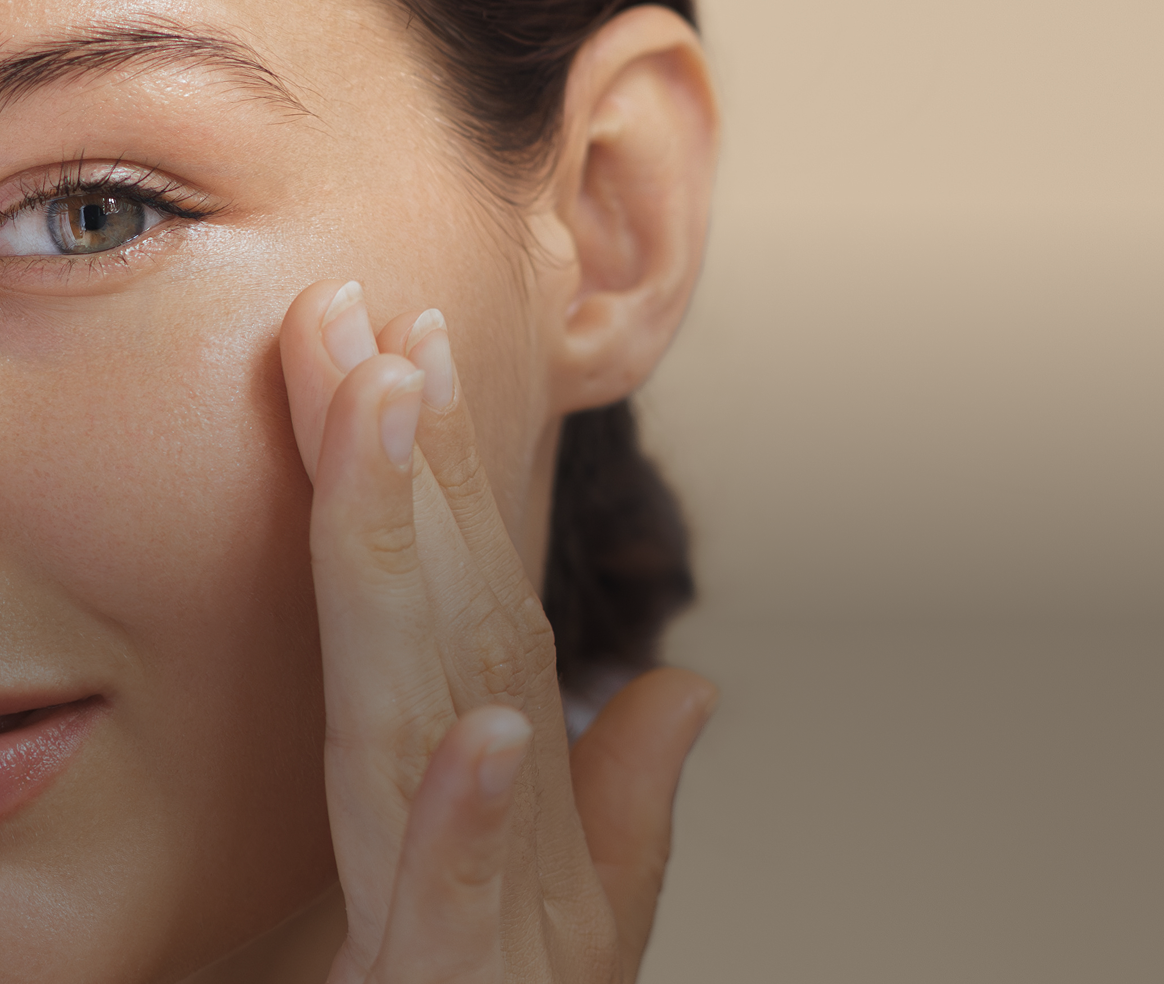 A close-up of a woman gently touching the skin under her eye with her fingers.