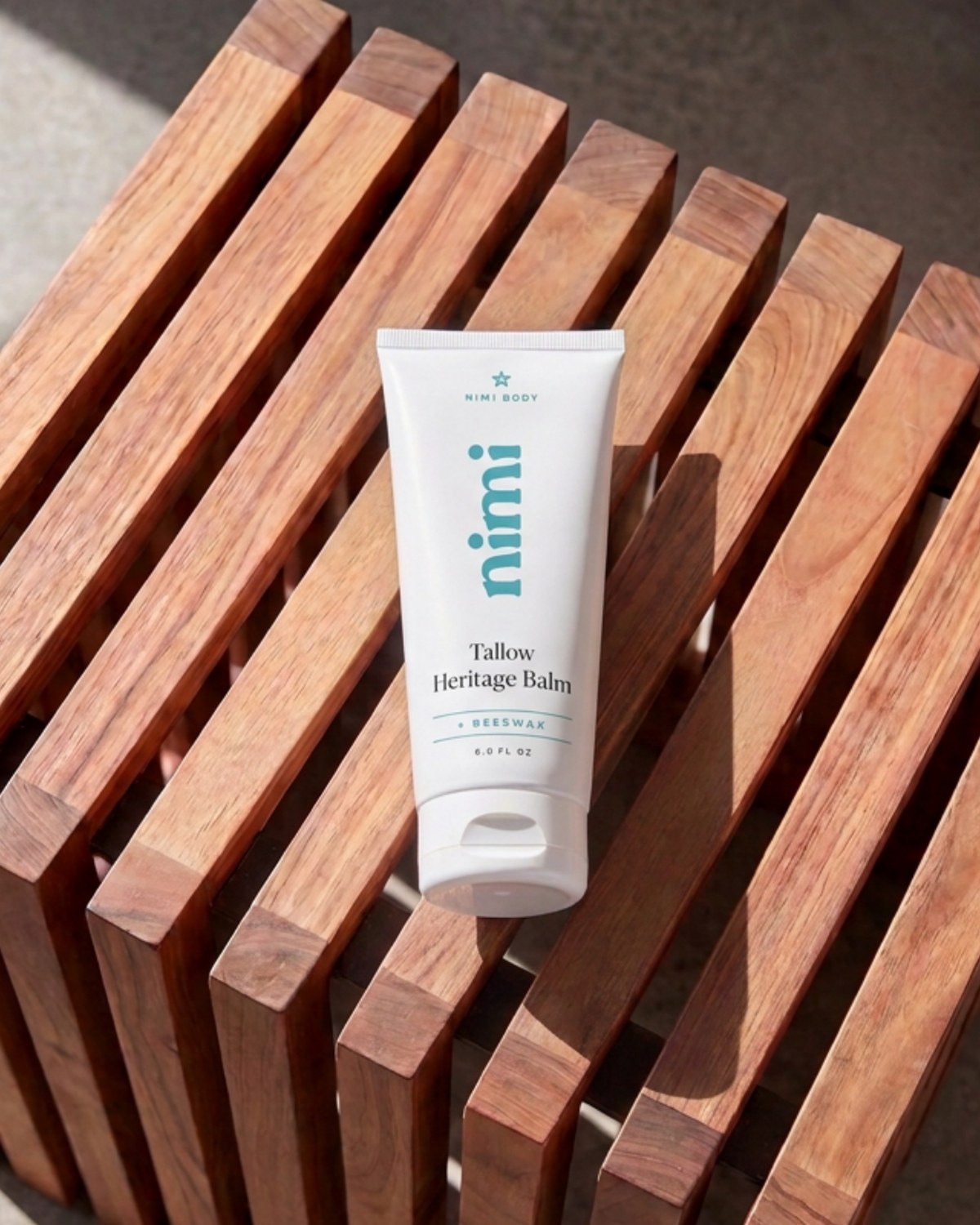 A white pump bottle of Nimi body wash resting diagonally on a slatted wooden bench.
