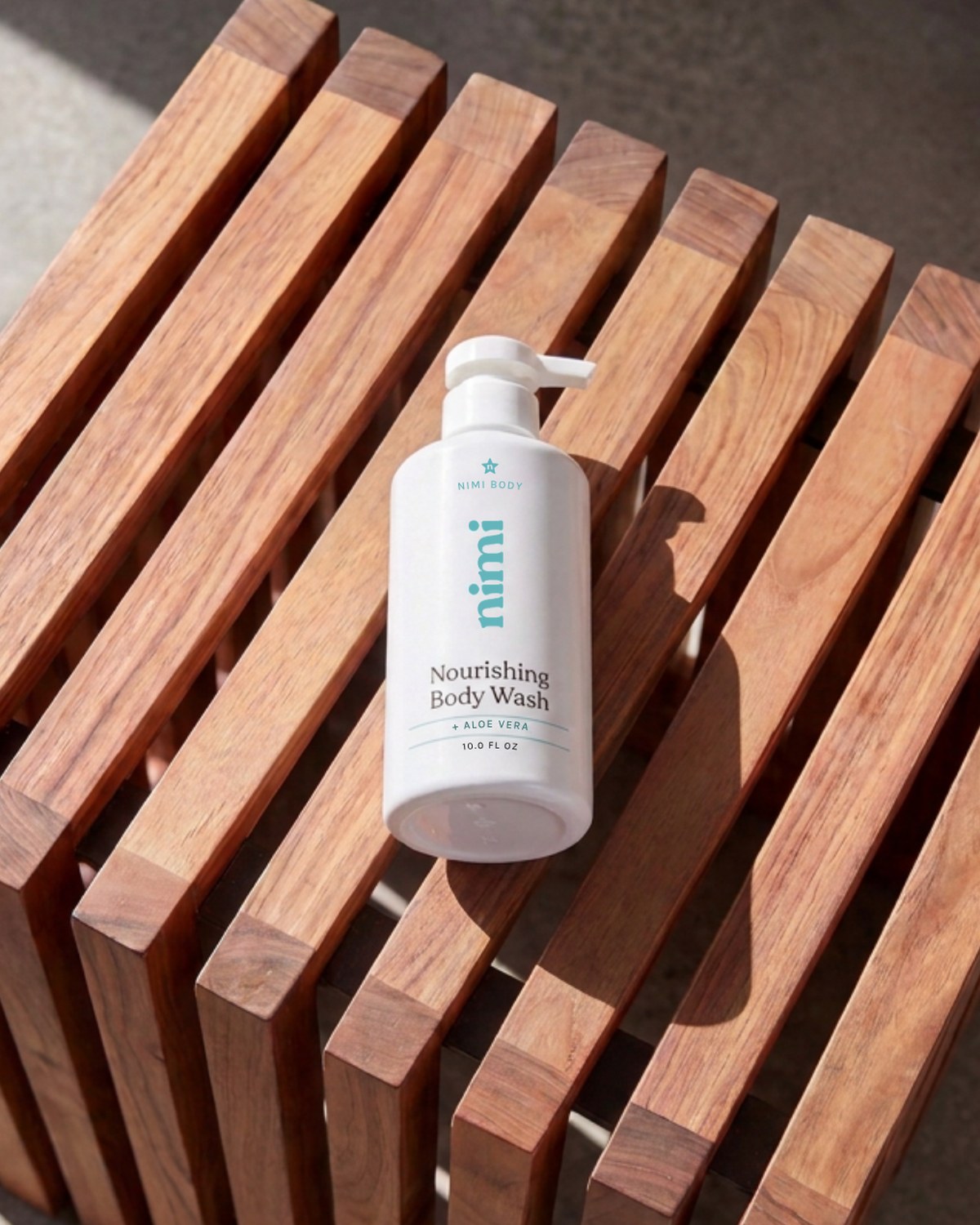 A white pump bottle of Nimi body wash resting diagonally on a slatted wooden bench.