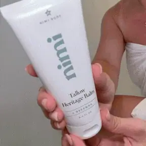 A person's hands holding a white tube of Nimi Tallow Heritage Balm.