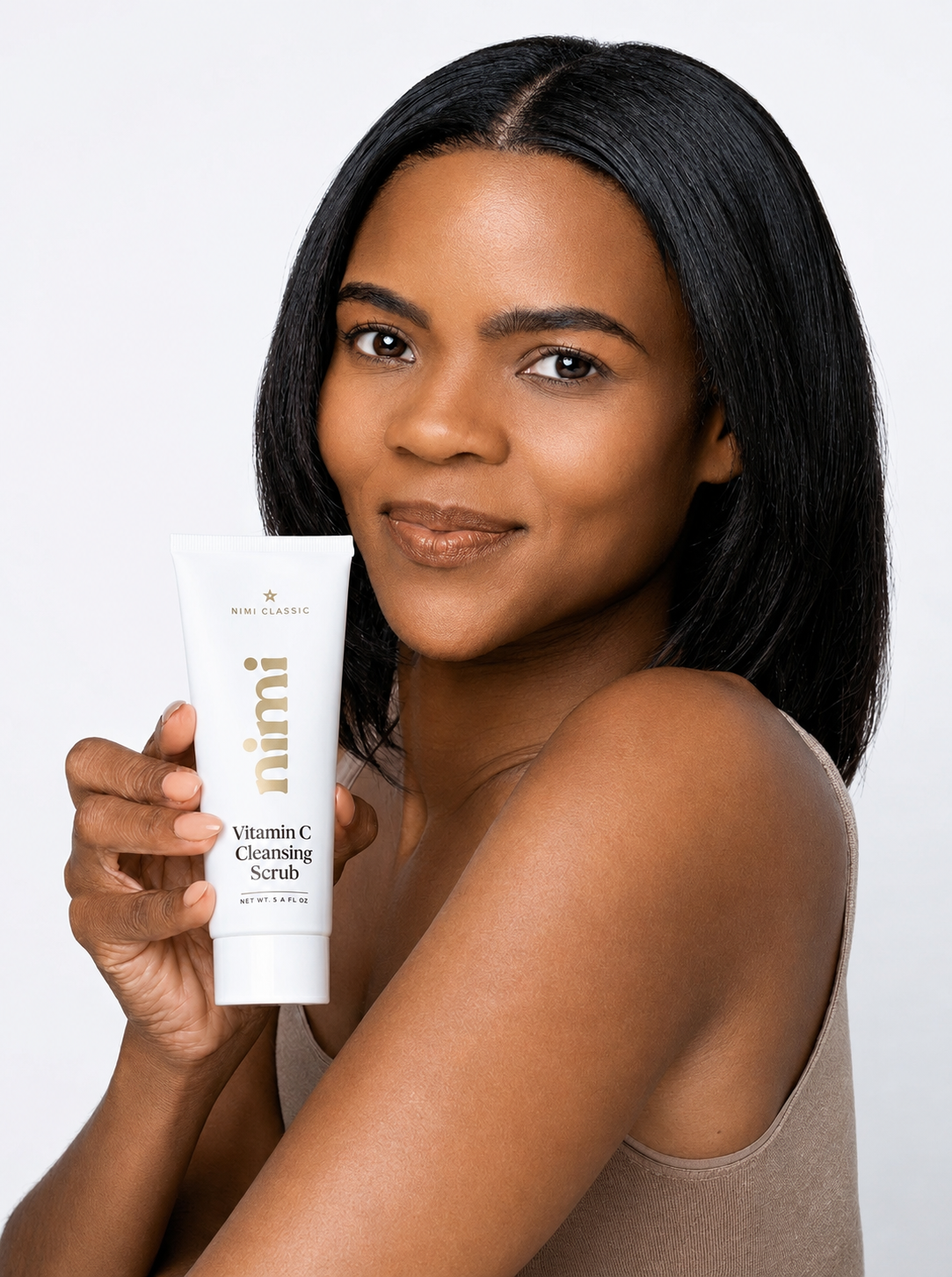 A woman with dark hair holds up a white tube of Nimi Vitamin C Cleansing Scrub.