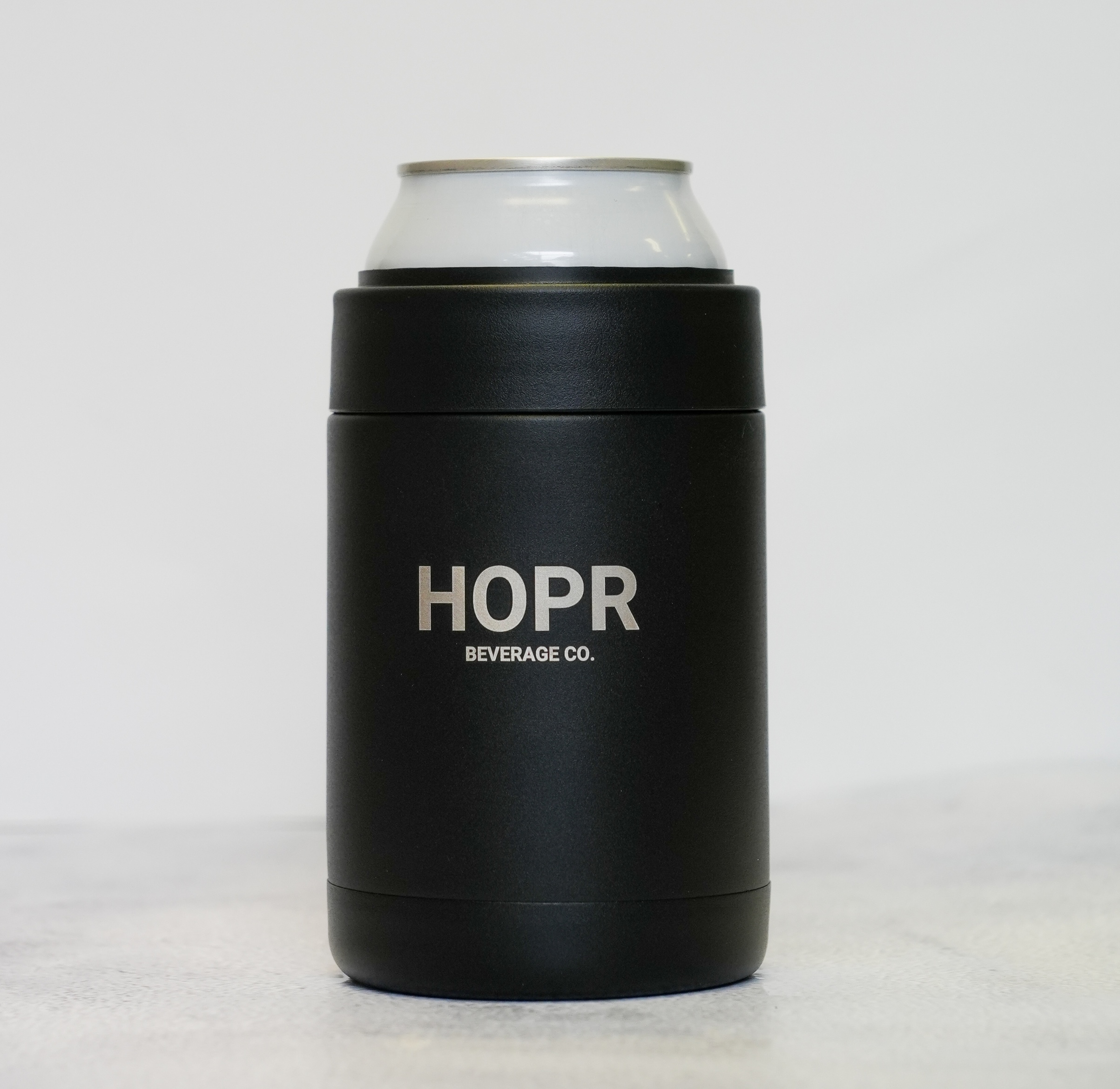 A black HOPR Beverage Co. can insulator with the top of a beverage can sticking out.