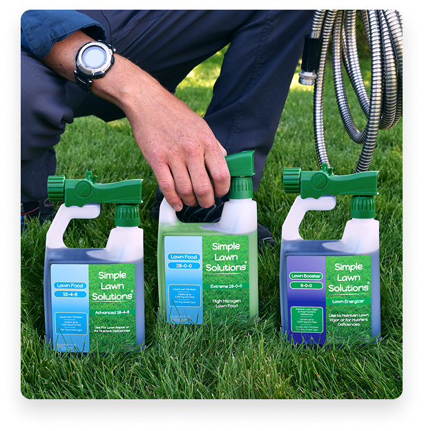 Three lawn care spray bottles on grass with a person's hand and hose.