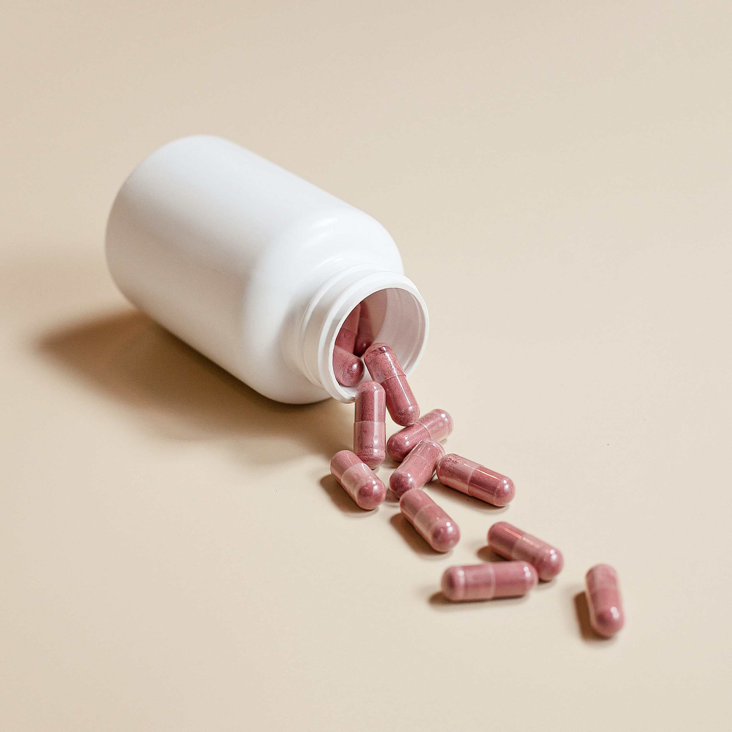 White bottle with pink capsules spilling out on a beige surface.
