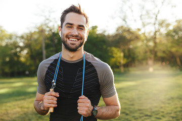 Smiling man holding a jump rope outdoors on a sunny day.