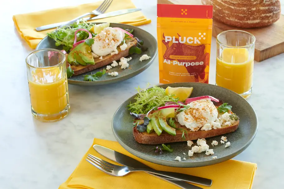 Two plates of avocado toast with poached eggs, orange juice, and a Pluck All-Purpose seasoning pack.