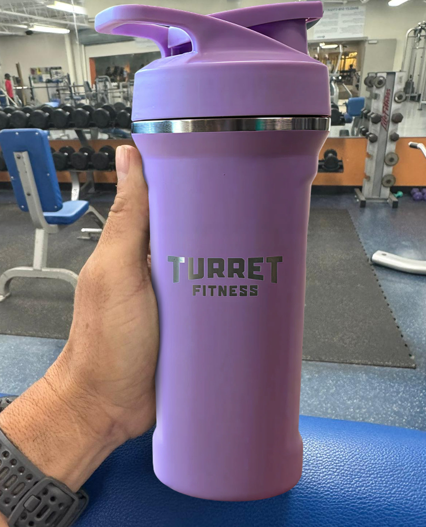 Purple fitness shaker bottle with 'Turret Fitness' in a gym.