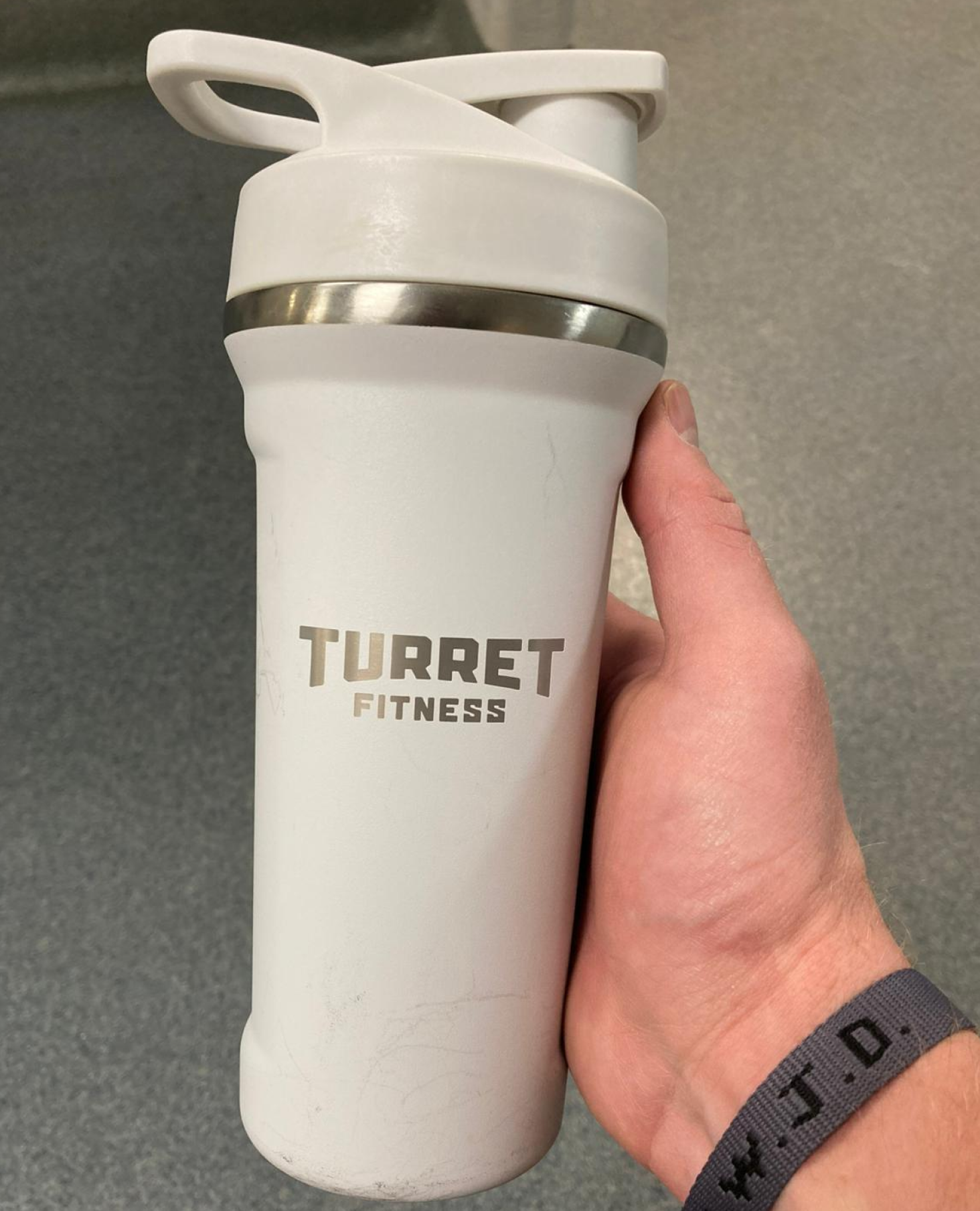A white Turret Fitness shaker bottle held in a hand.