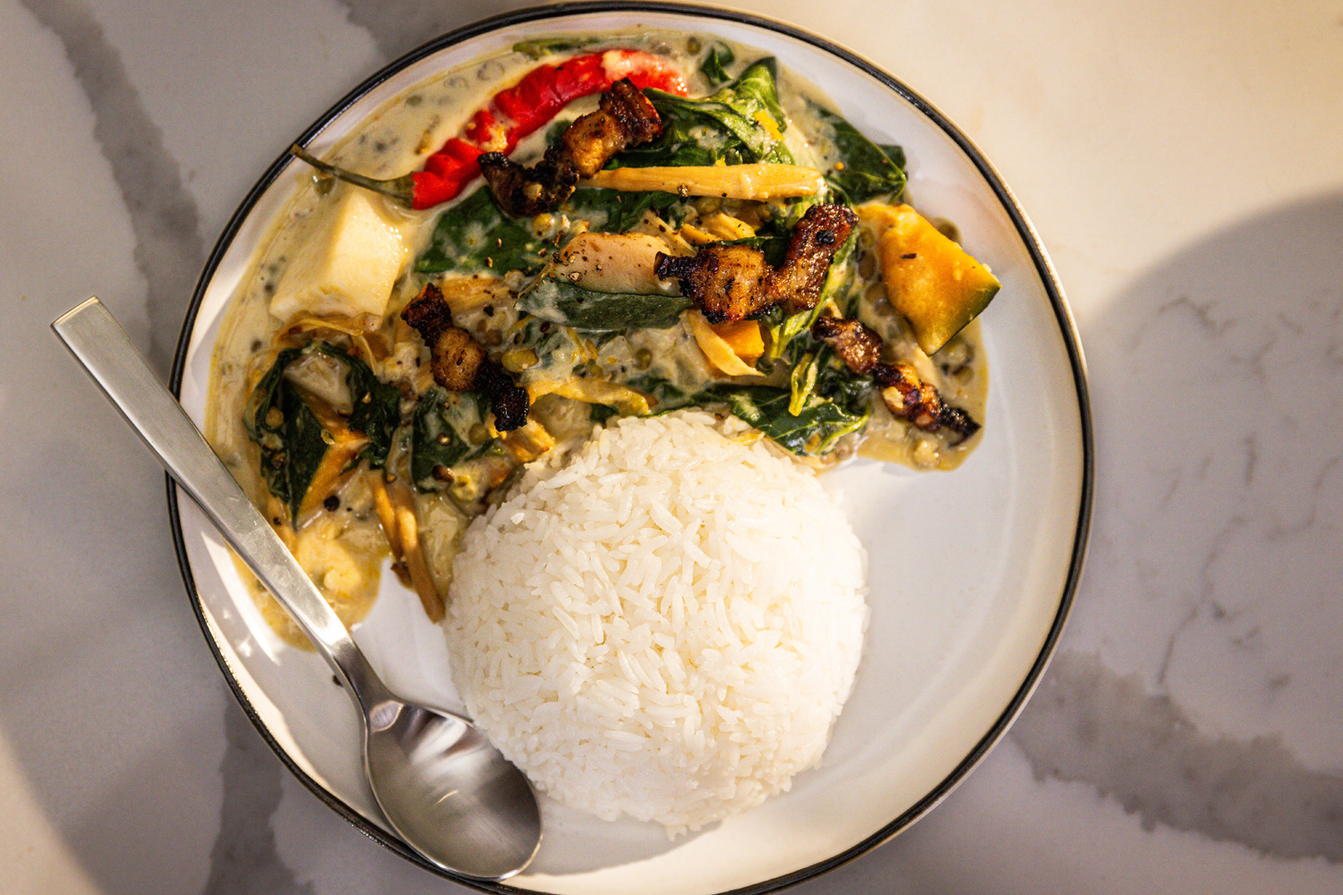 Plate of rice with vegetables and grilled meat, served with a spoon.