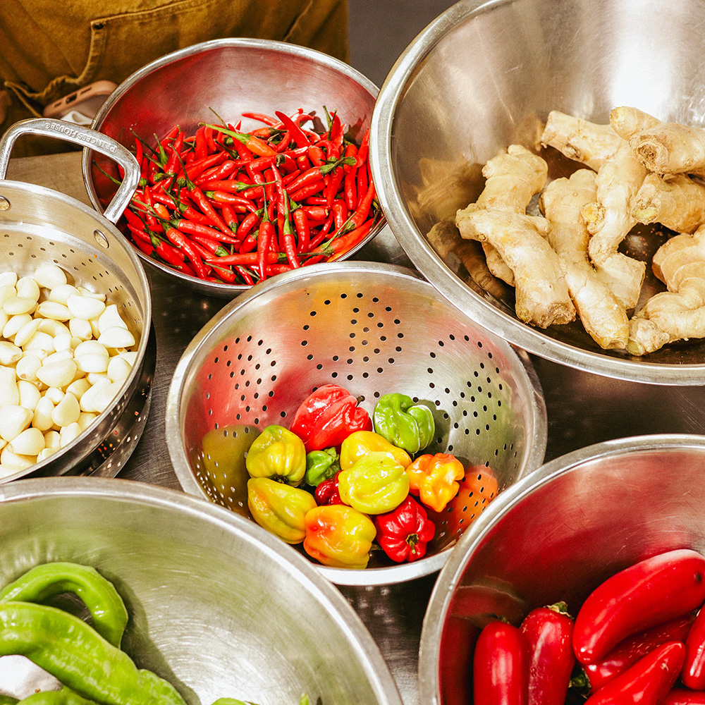 Assorted fresh peppers, garlic, and ginger in metal bowls on a kitchen counter.