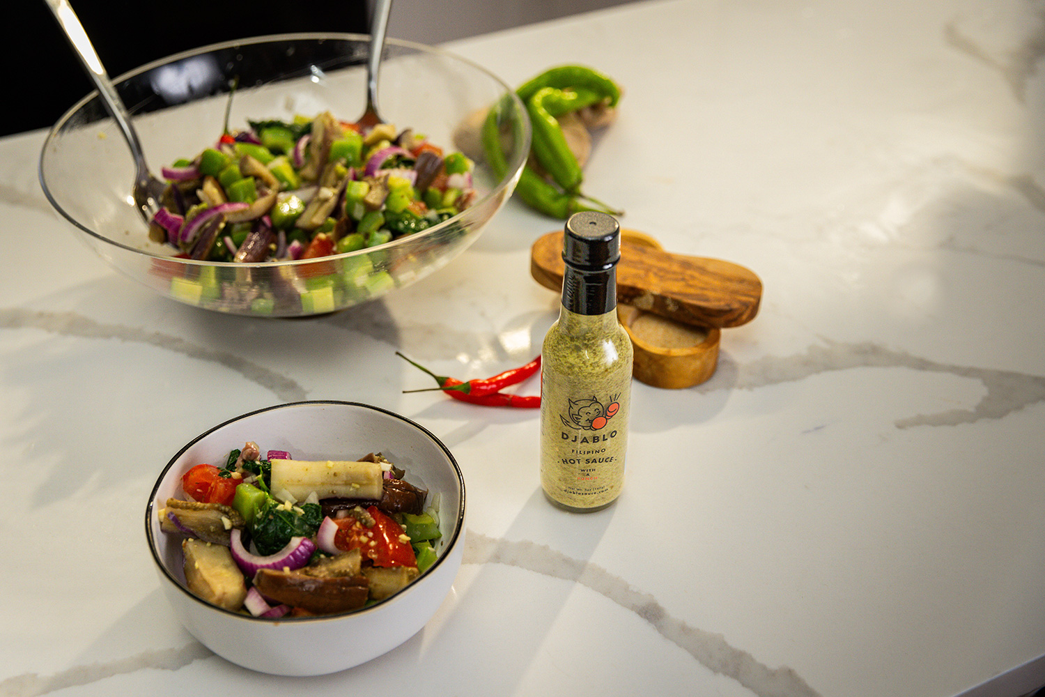 Salad in bowls with hot sauce bottle on a marble countertop.