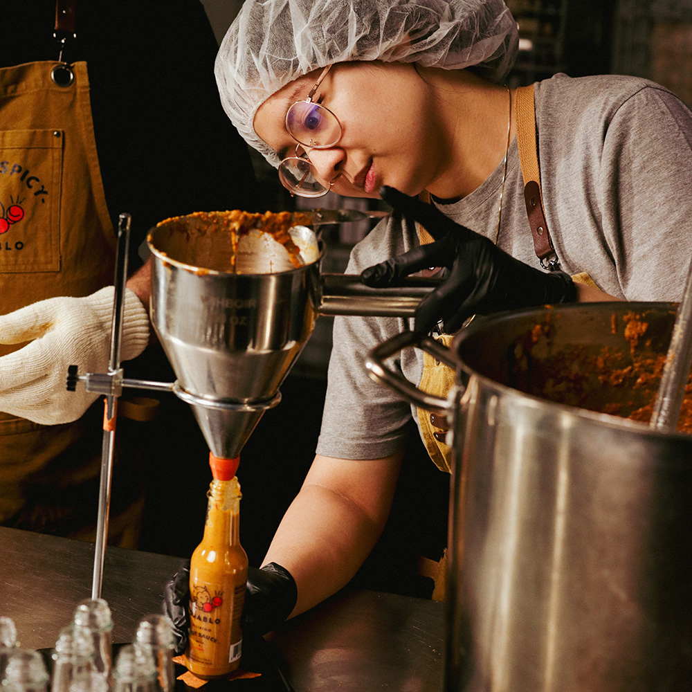 Person bottling sauce using a funnel in a kitchen setting.