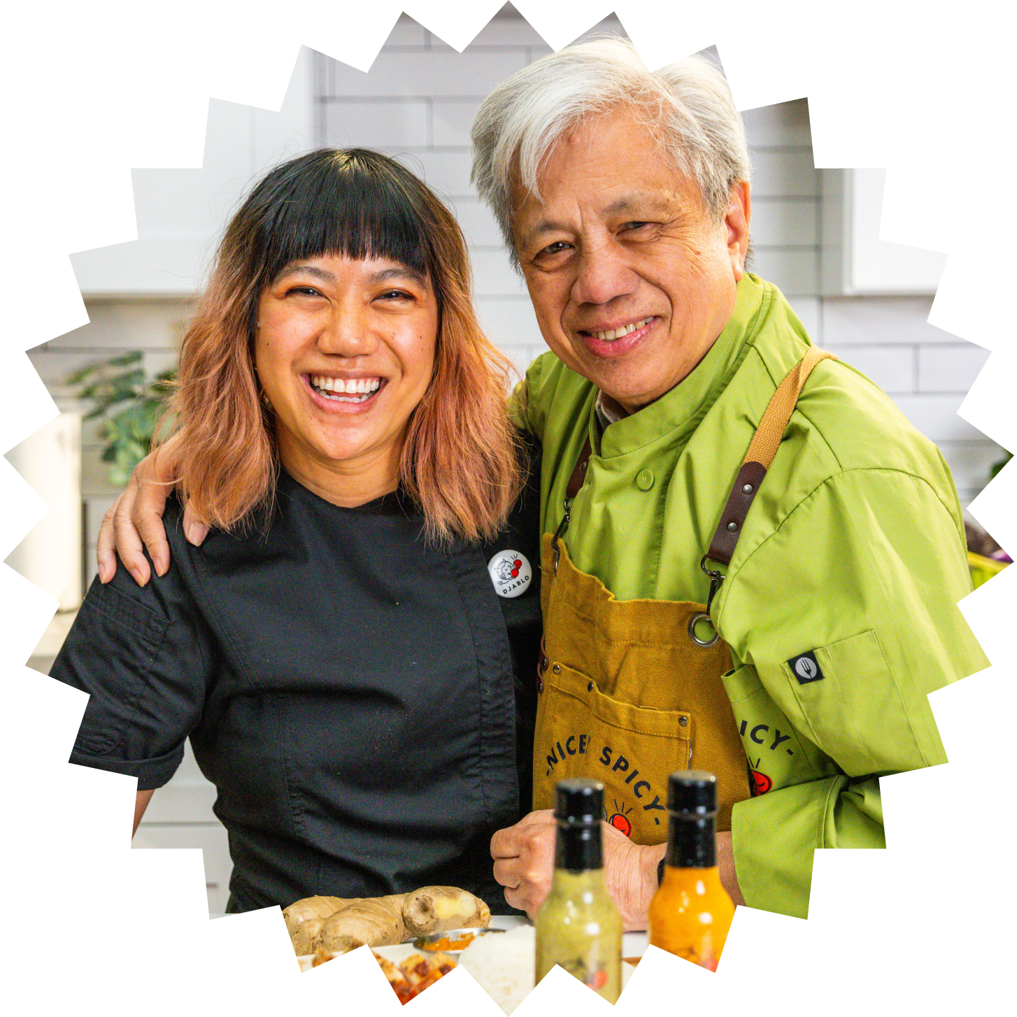 Two chefs smiling together in a kitchen, with spice bottles in the foreground.